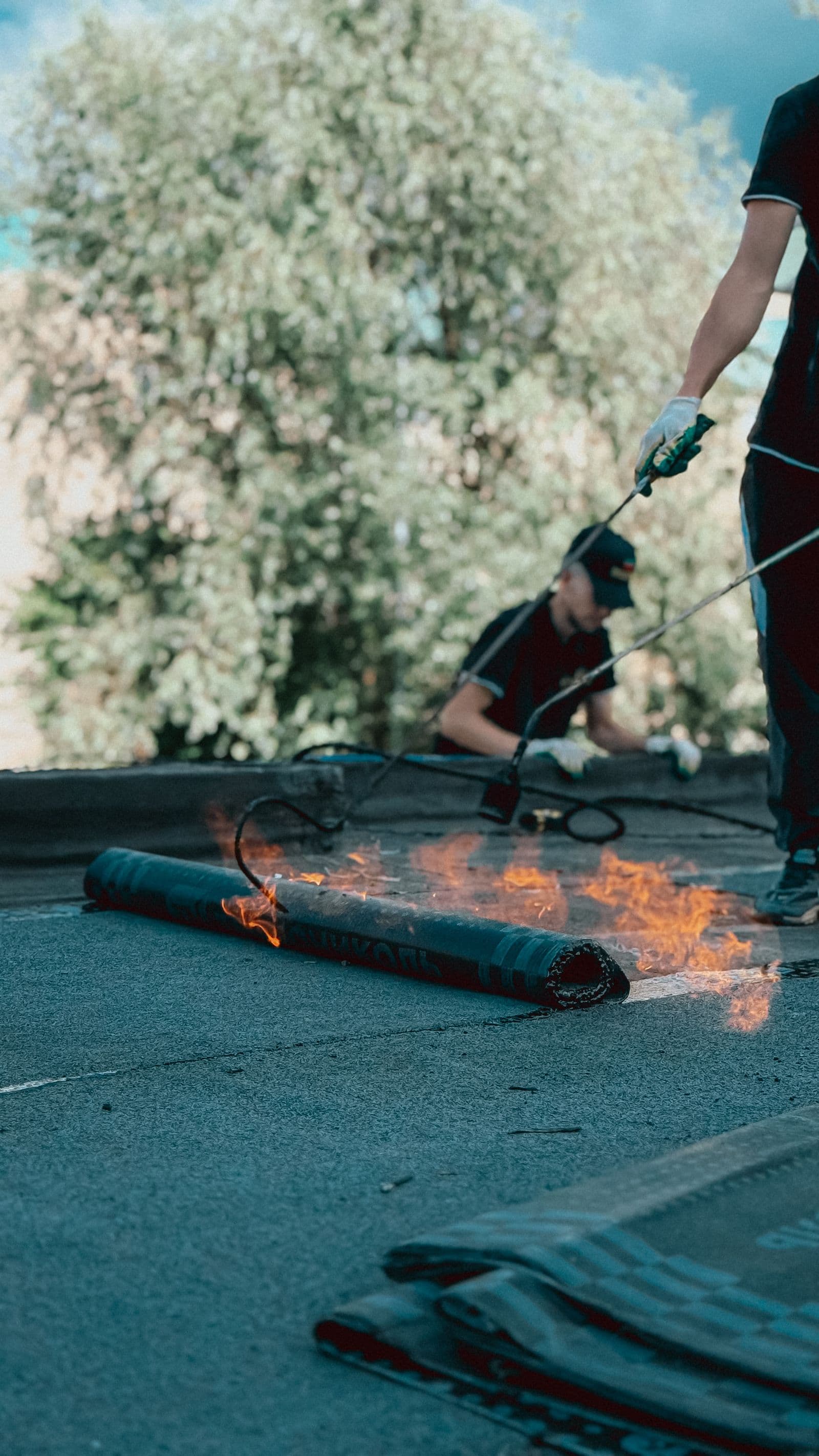 Roofer torching down a modified bitumen roll on a flat commercial roof