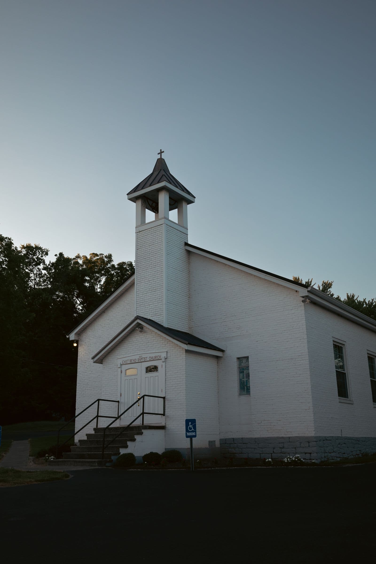 White clapboard church with a steeple, surrounded by trees
