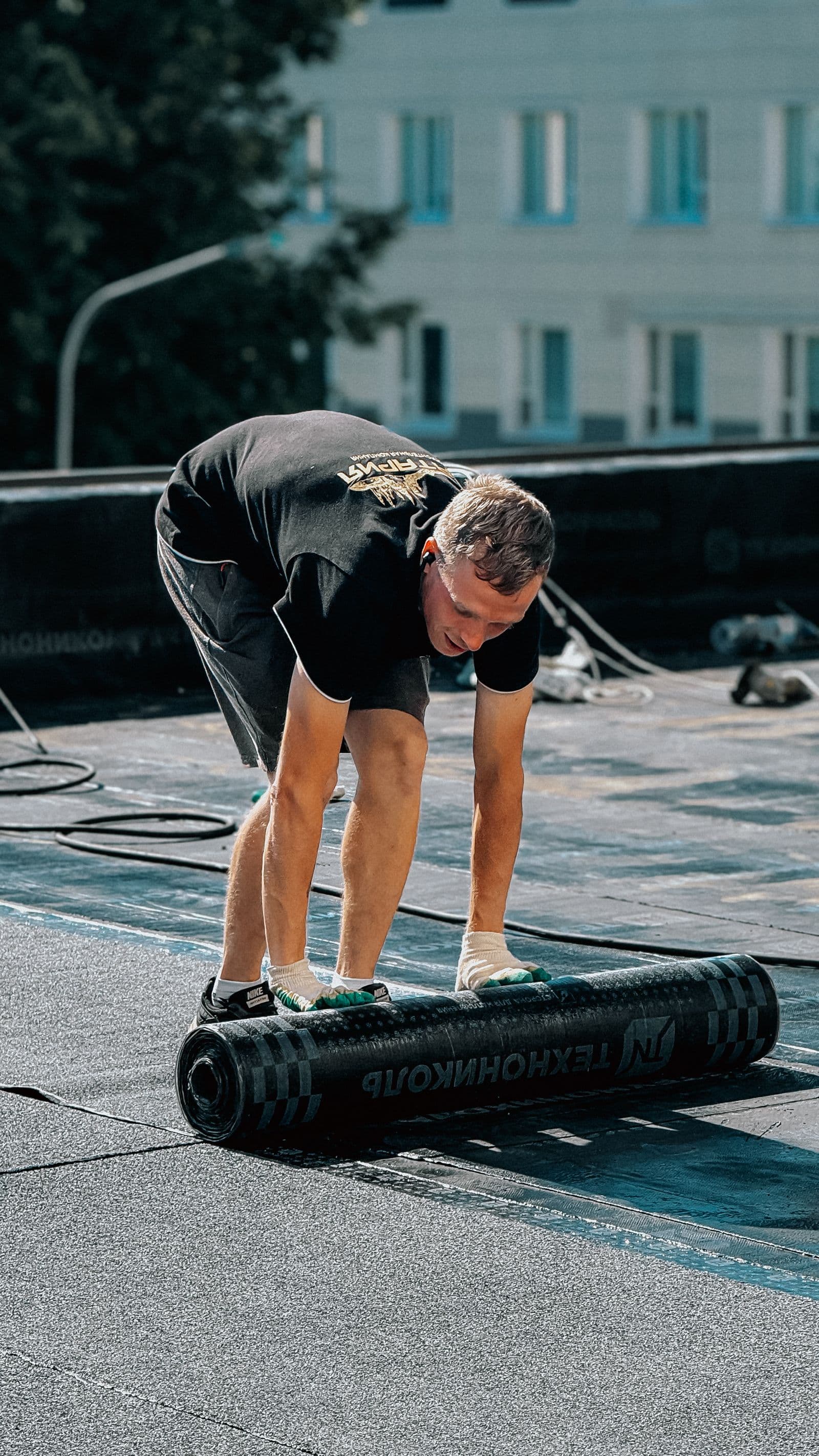 Roofer unrolling a black rubber membrane across a flat commercial roof