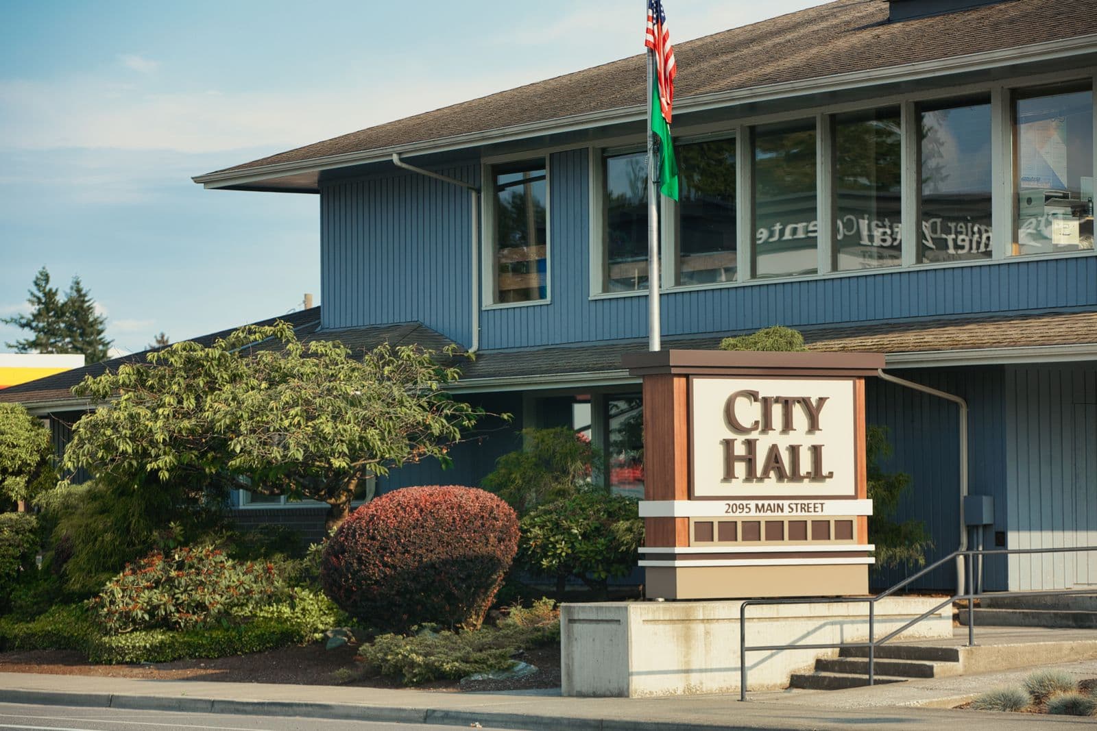 Municipal city hall building behind a landscaped sign and flagpole