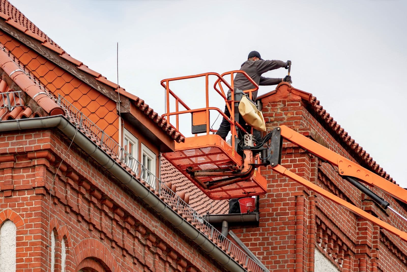 Roofer on an elevated lift inspecting the roofline of a brick commercial building
