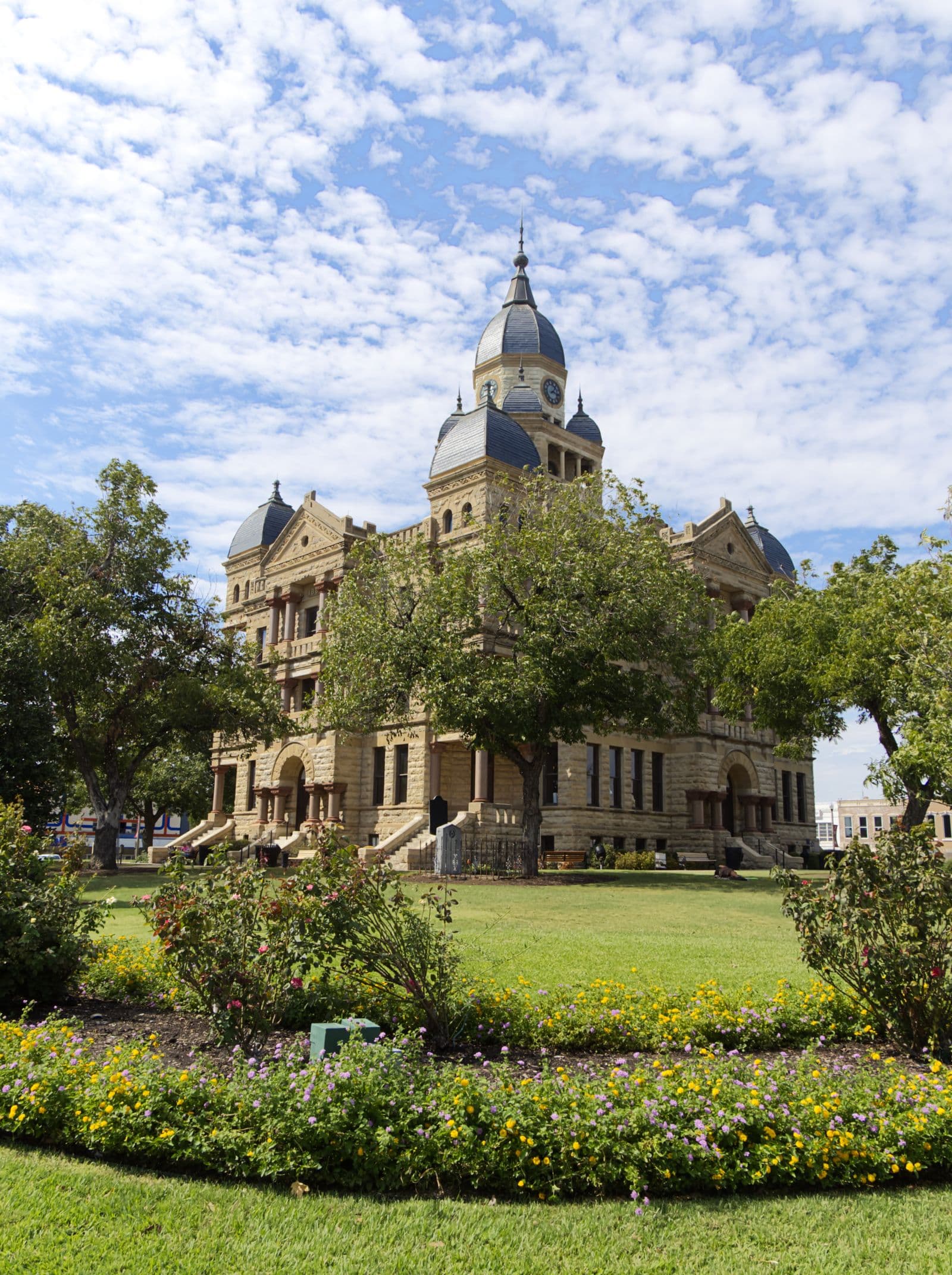 Stone county courthouse with a clock tower, set back behind lawn and trees