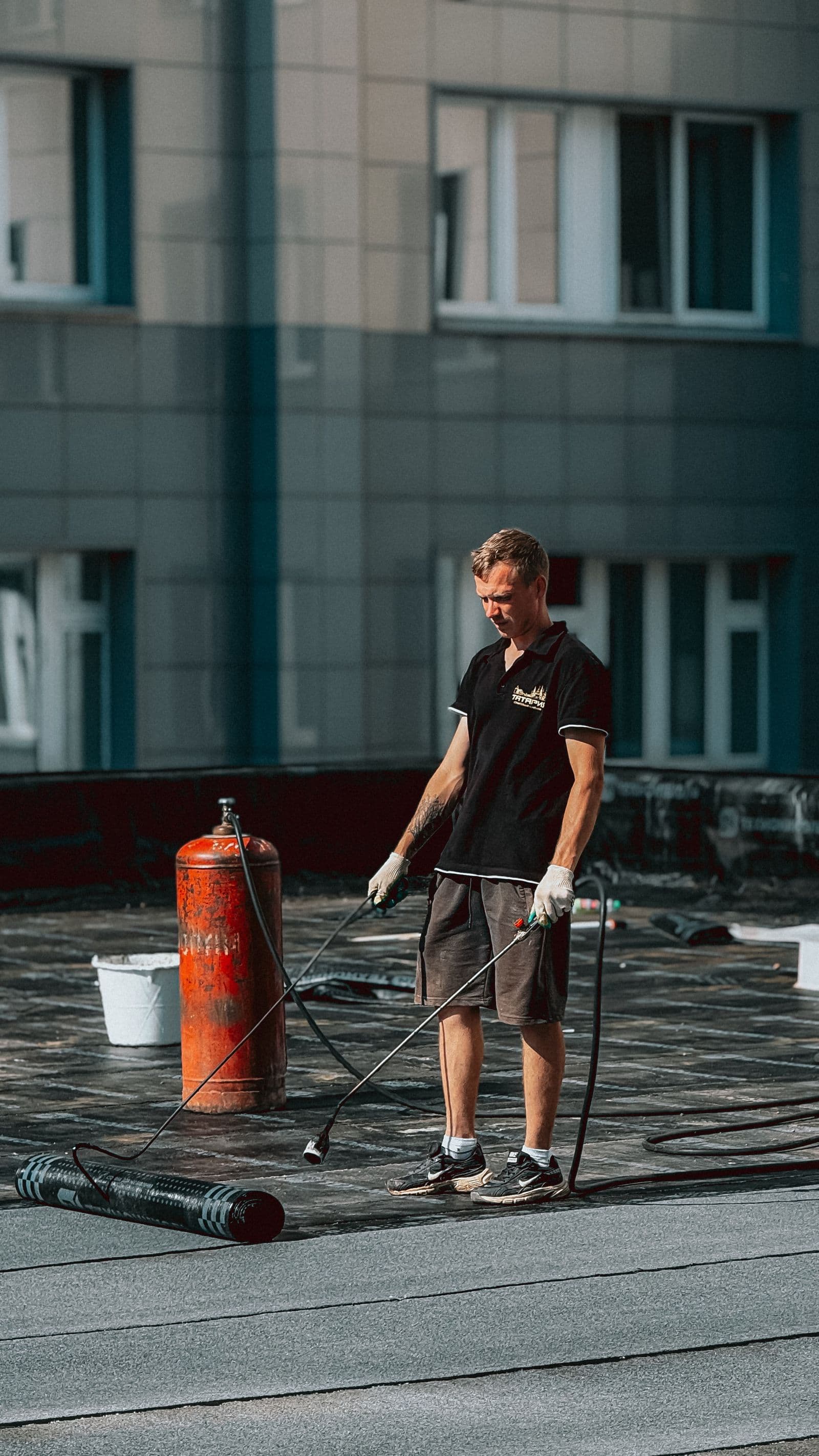 Roofer working across a large flat roof beside an institutional building